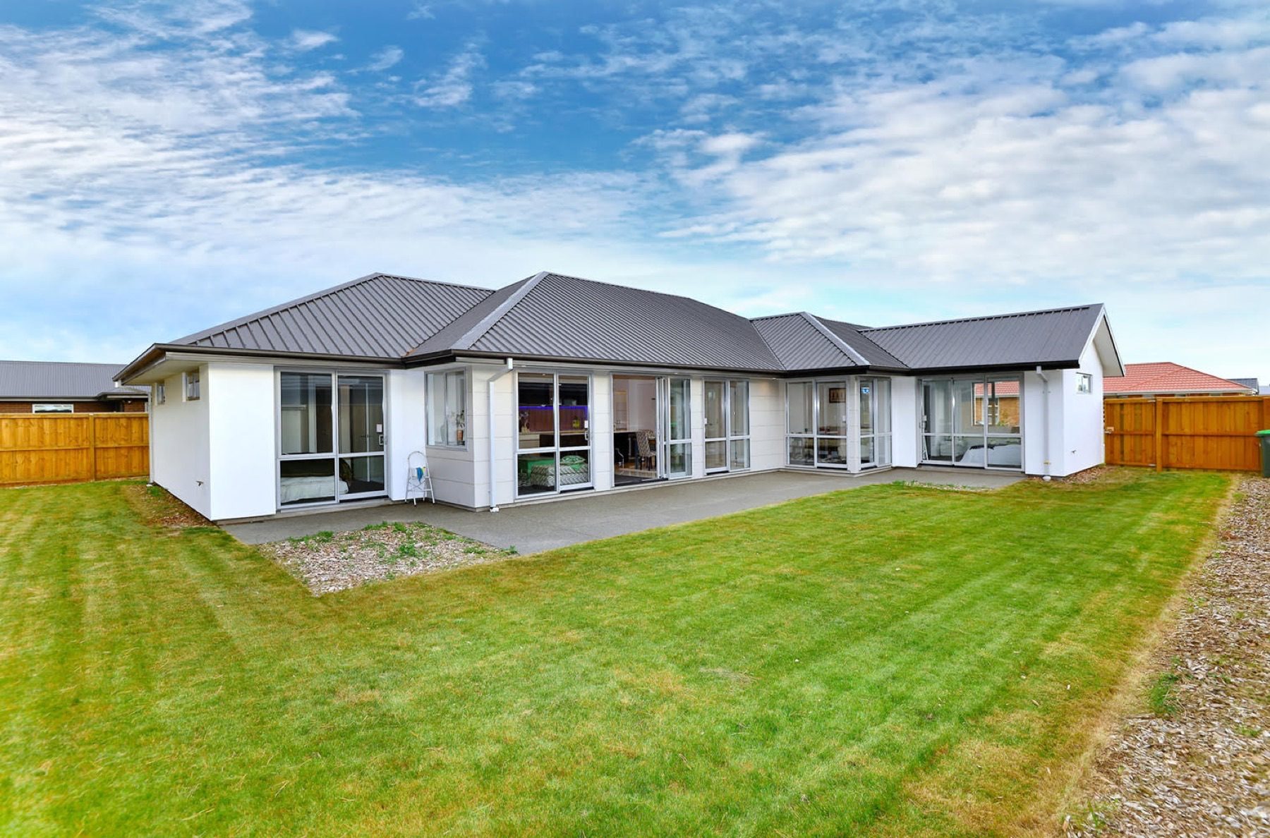 The rear of the Faringdon home, where the elevation folds around a wide concrete patio with sliding doors to the lawn.