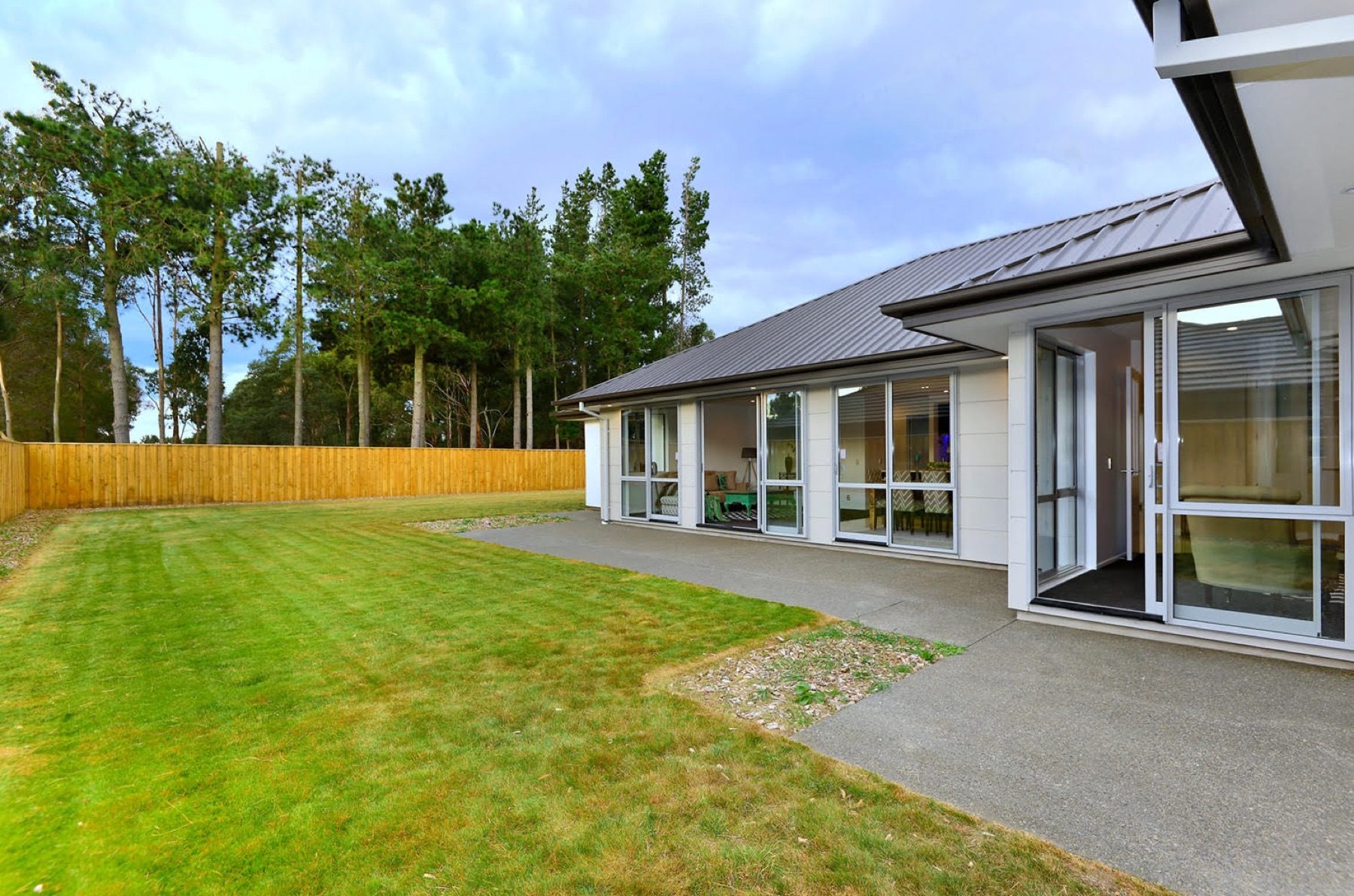 The Faringdon home from the back lawn, with the dark hip roof running the length of the elevation and pines beyond the boundary.