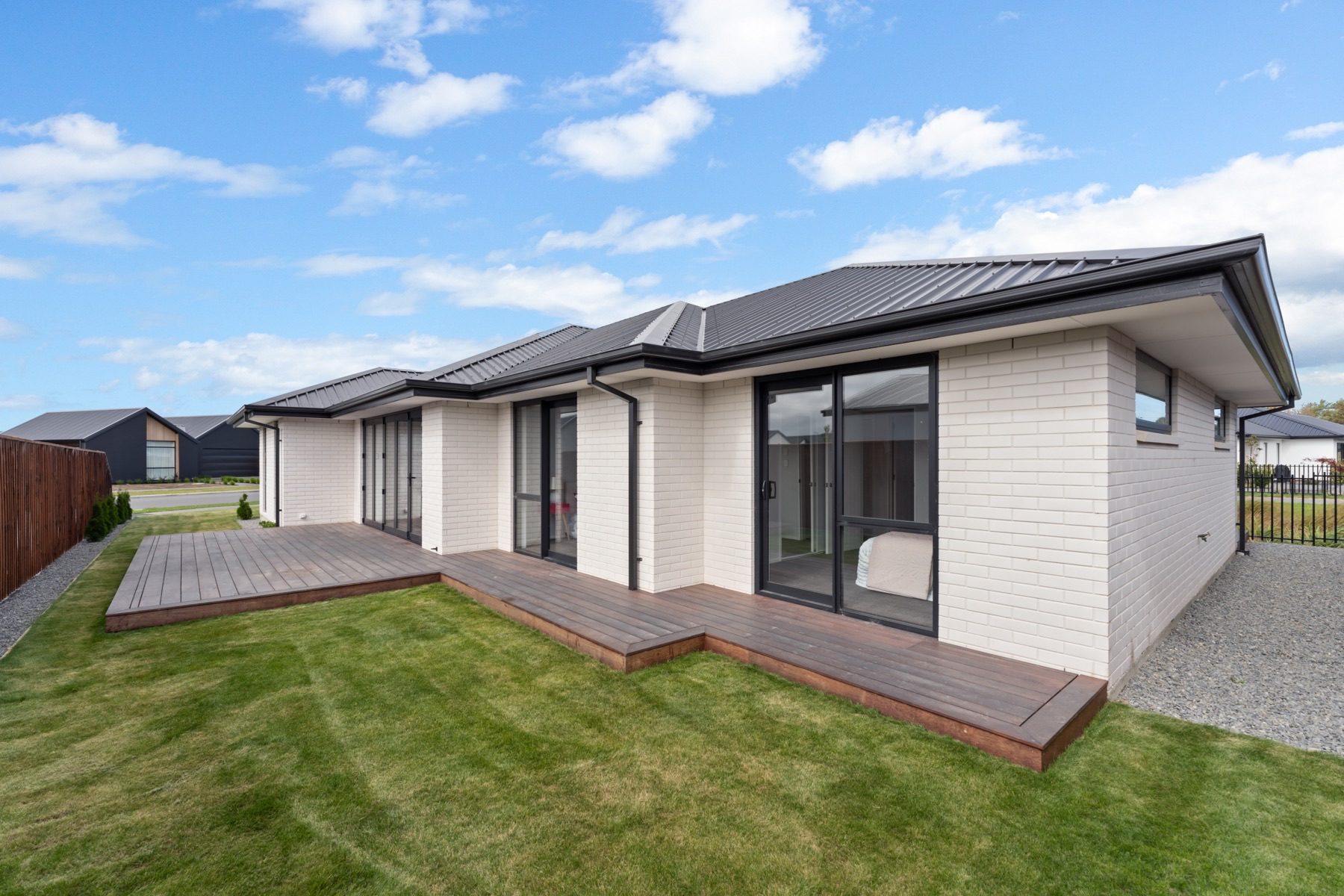 The rear of the Milns Park house, with the timber deck wrapping the corner past bedroom sliders and the reserve boundary railing at right.