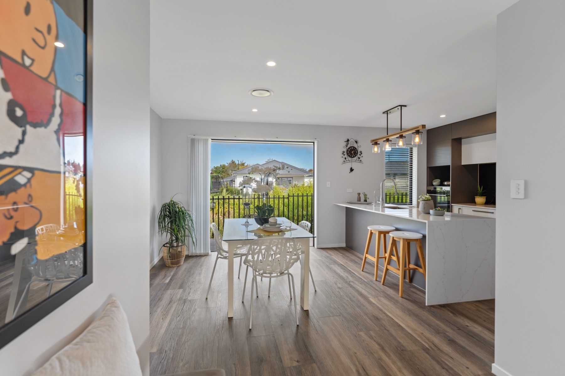 Dining beside the kitchen at Milns Park, with a marble-look stone breakfast bar, a waterfall end and the slider open to the reserve boundary.