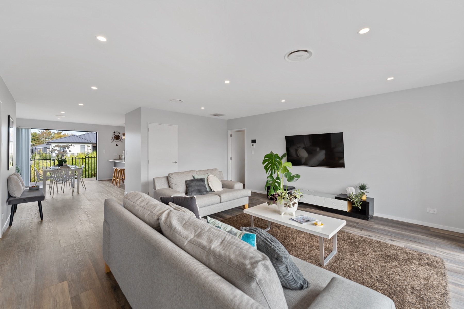The full open-plan run at Milns Park: living in the foreground, with dining and the kitchen at the far end where the slider opens to the reserve.