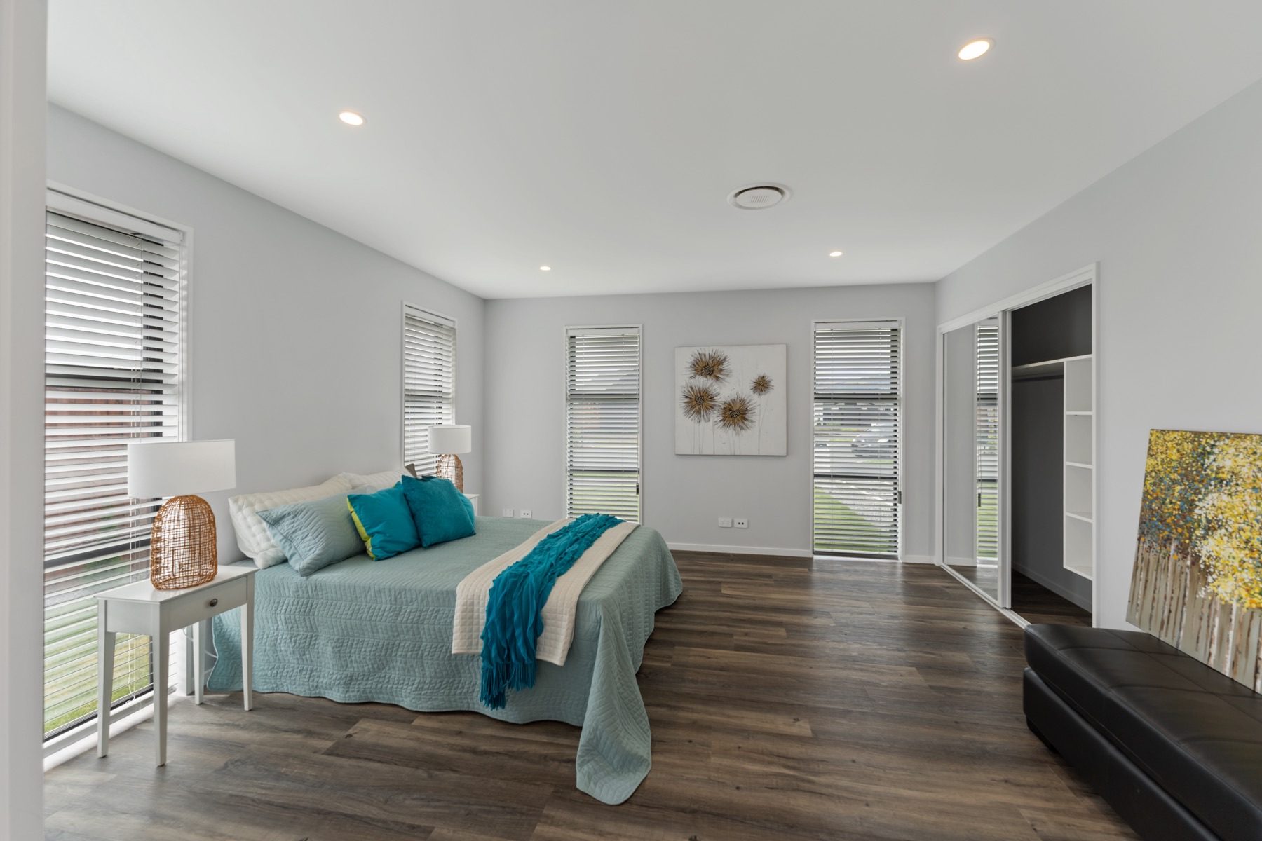 The main bedroom, lit by tall windows on two walls, with a walk-in wardrobe through the sliding door beyond.