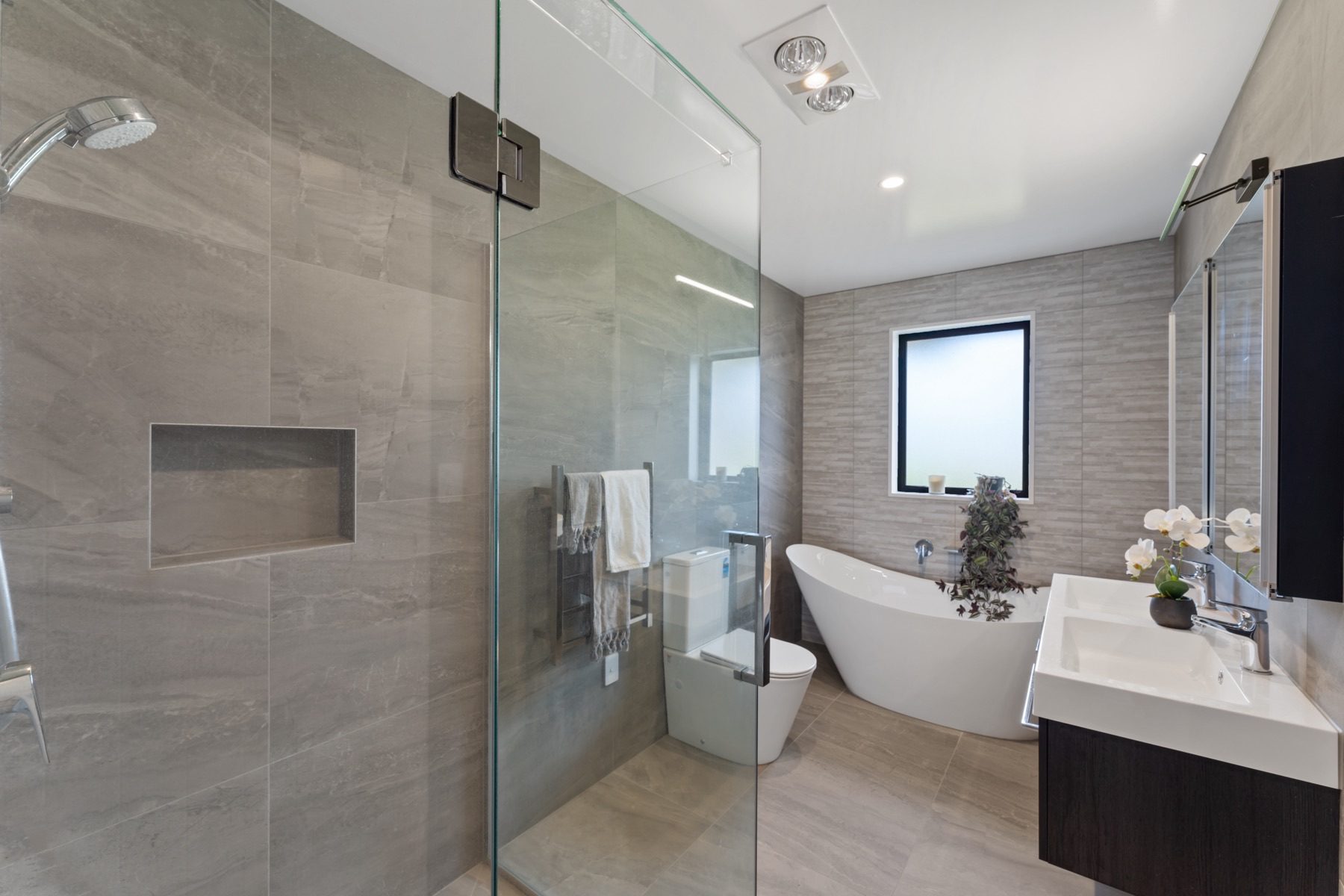 The fully tiled family bathroom, with a frameless glass walk-in shower, a freestanding bath and a dark timber double vanity.