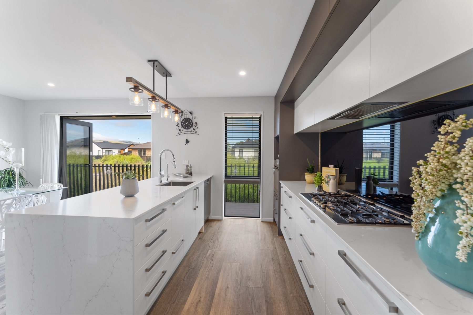 The Milns Park kitchen along its full length, with the gas cooktop and integrated rangehood on the right and the Port Hills through the open slider.