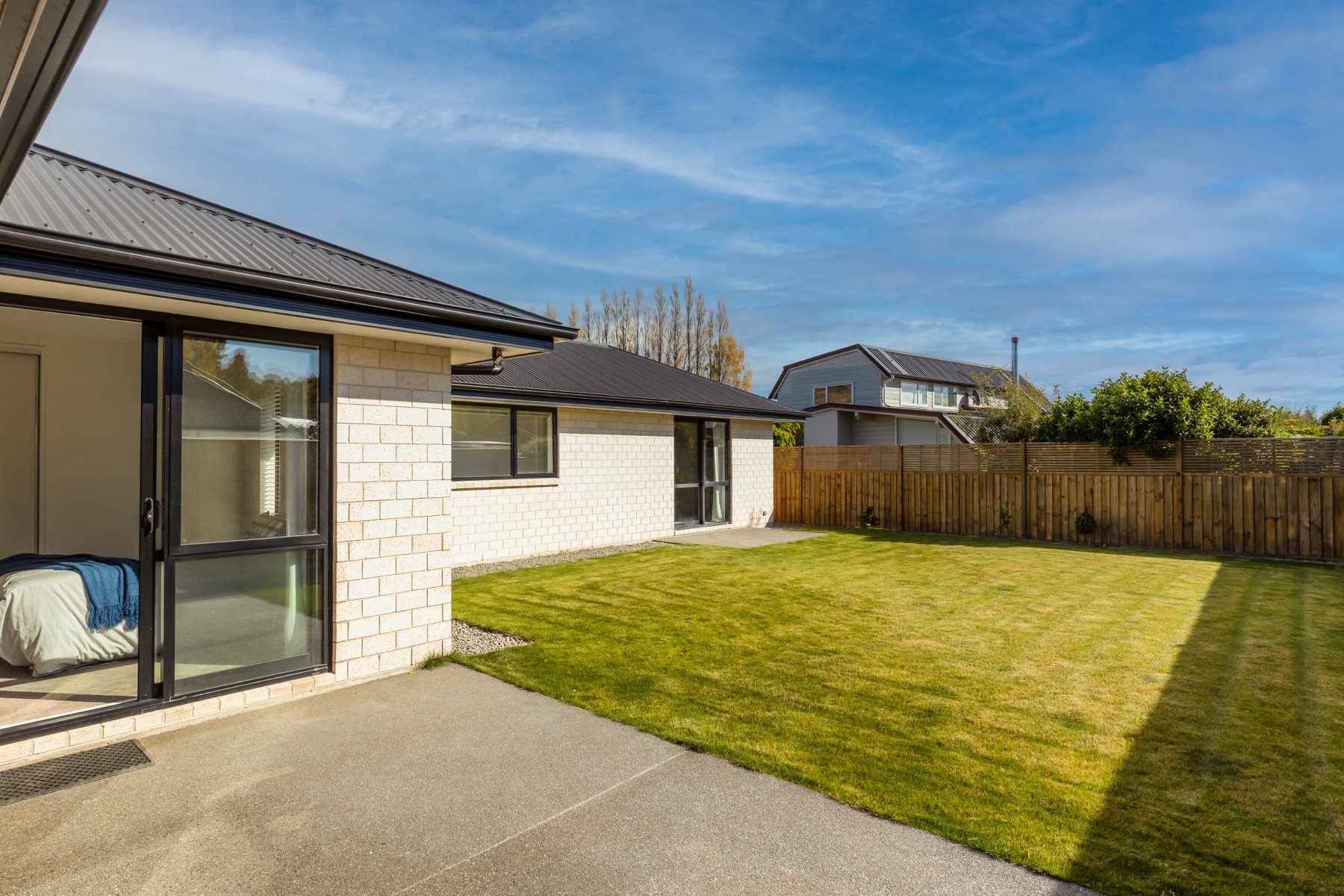 The concrete patio outside a bedroom slider at Old Stone Lane, looking across the lawn to the timber boundary fence.