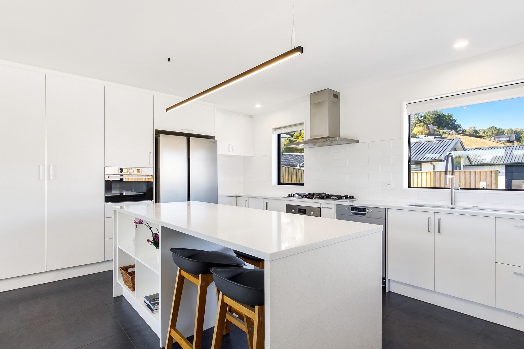 The Old Stone Lane kitchen from the dining end, with the island, wall oven and dark tiled floor.