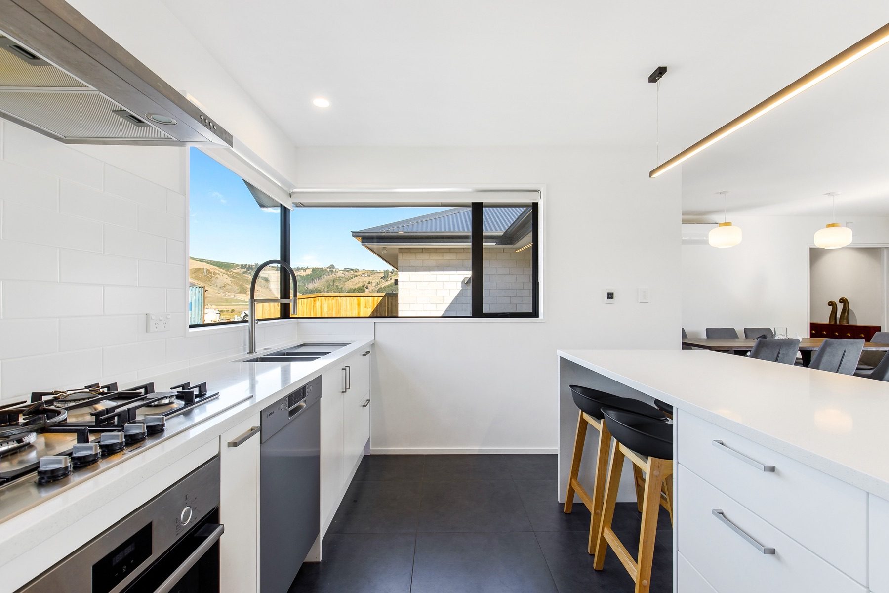 The kitchen's working run: a five-burner gas cooktop, wall oven, dishwasher and a double sink under a window looking to the hills.