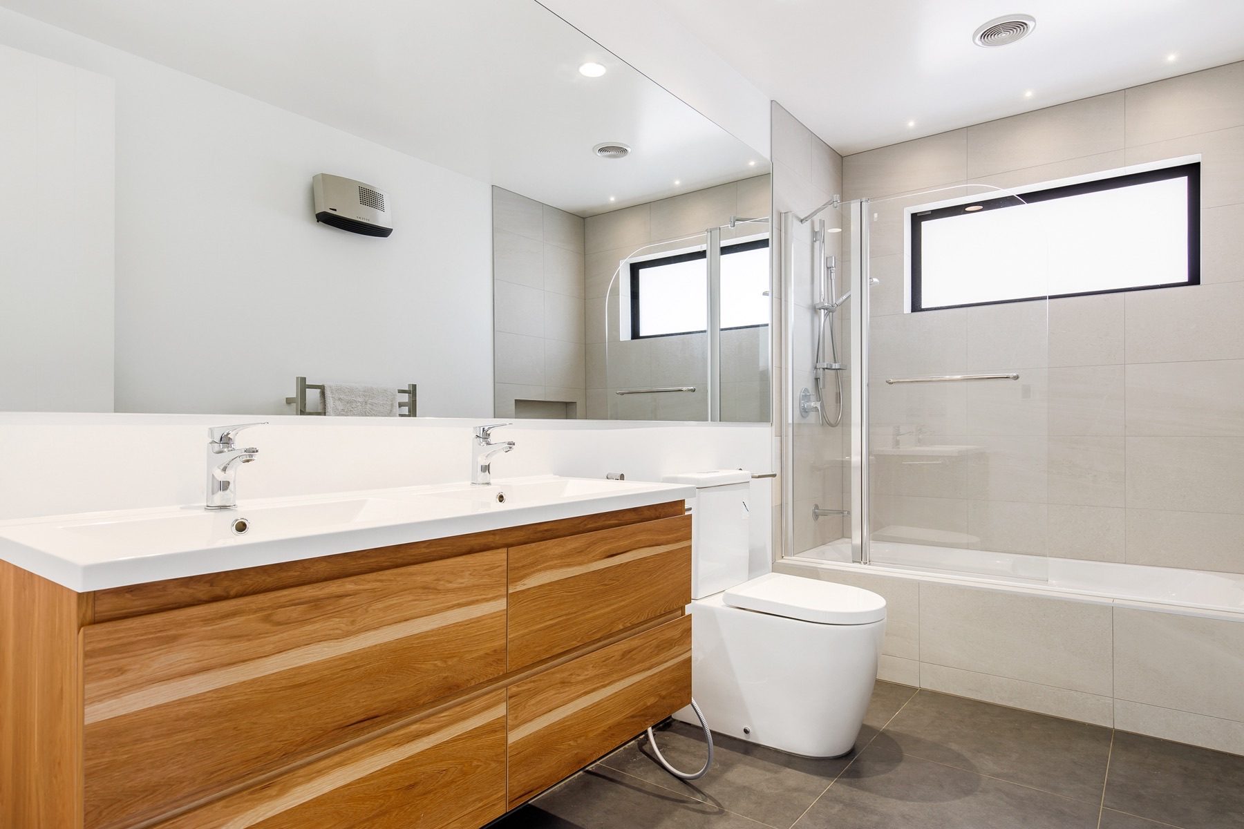 The family bathroom, with twin basins in a single top on a solid timber vanity, a full-width mirror and a bath with a glass screen.