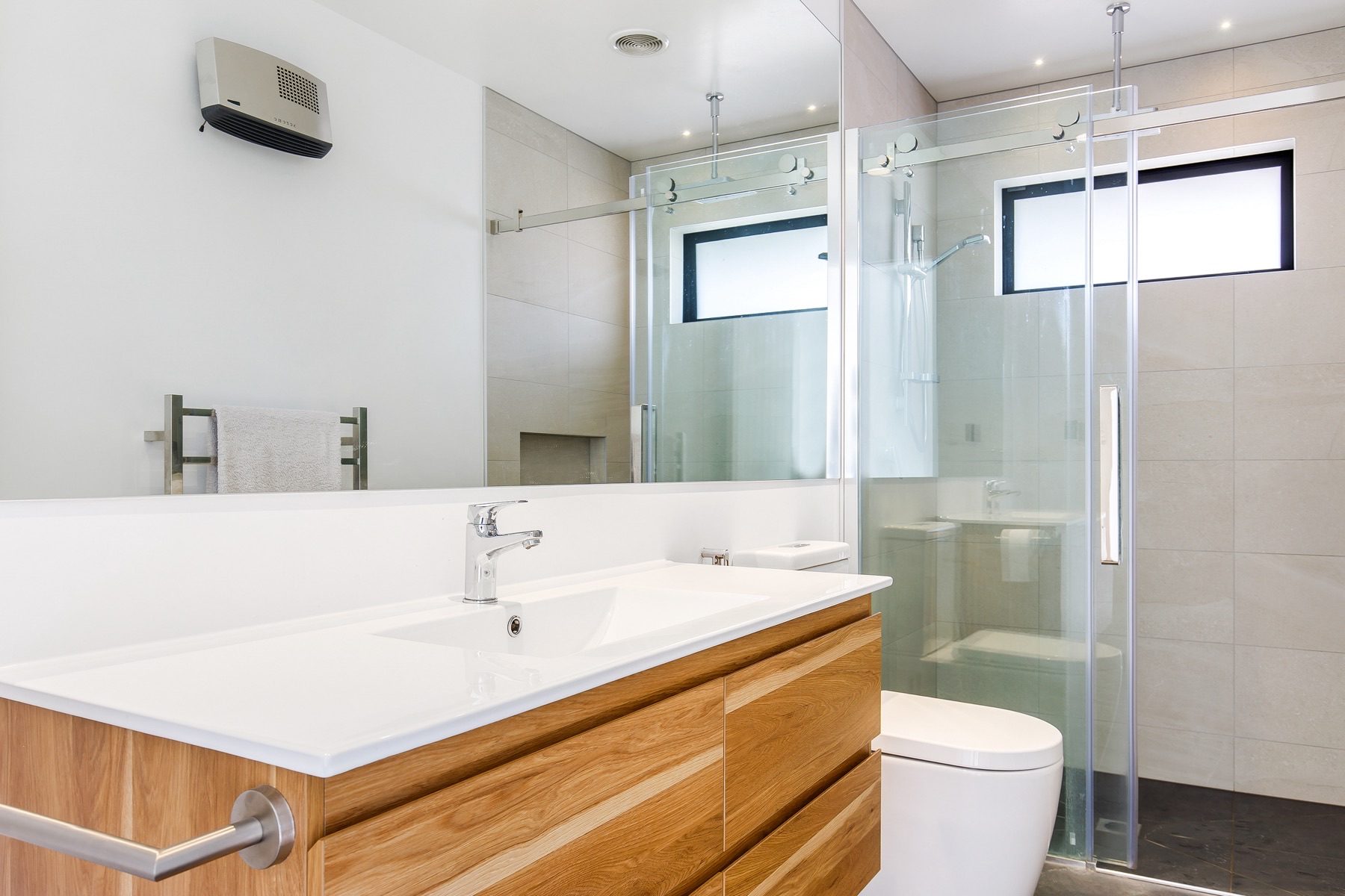 The ensuite, with a timber vanity, full-width mirror and a large sliding-glass shower under an overhead rain head.