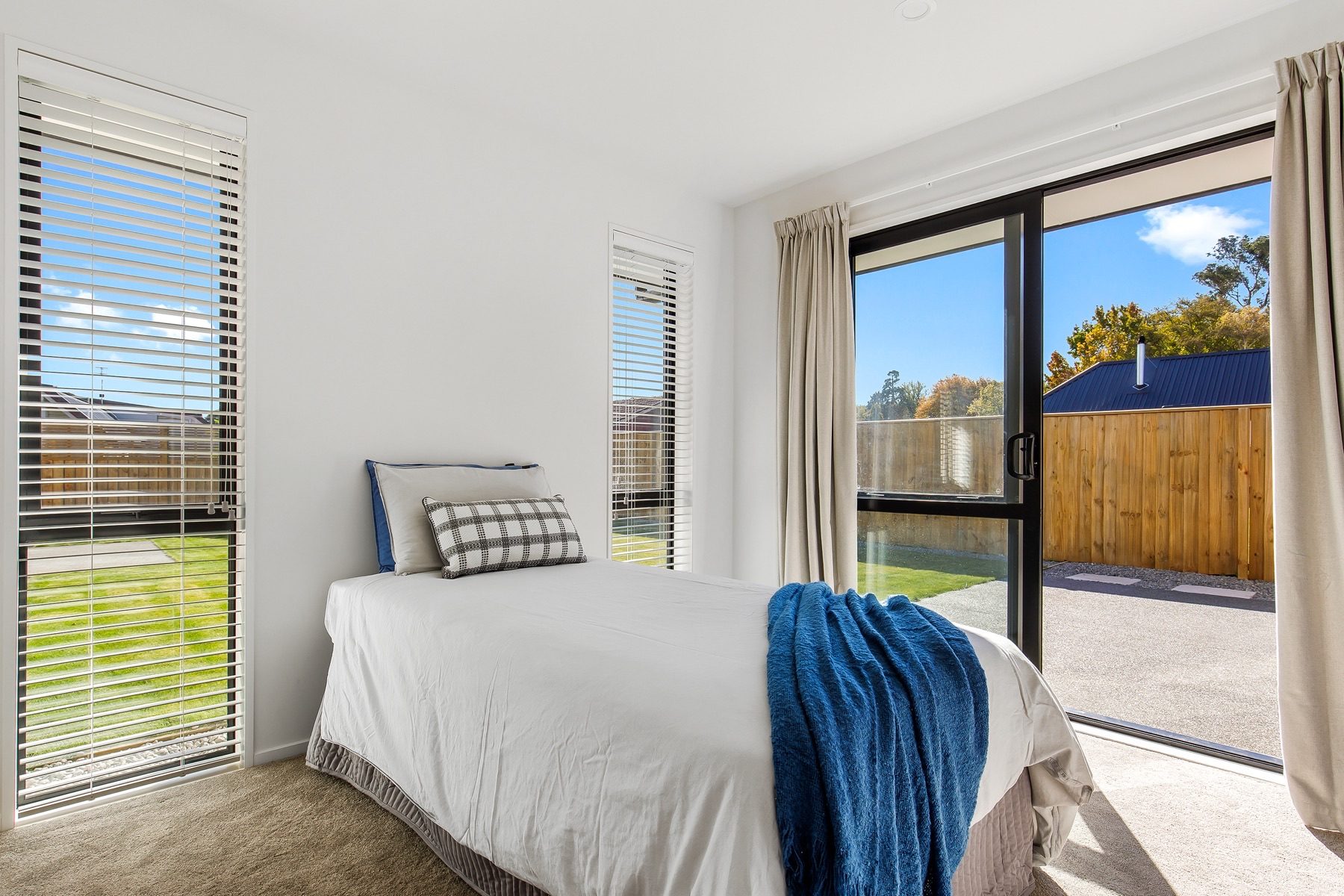 Bedroom with a sliding door onto the concrete patio and lawn, and a tall window alongside.