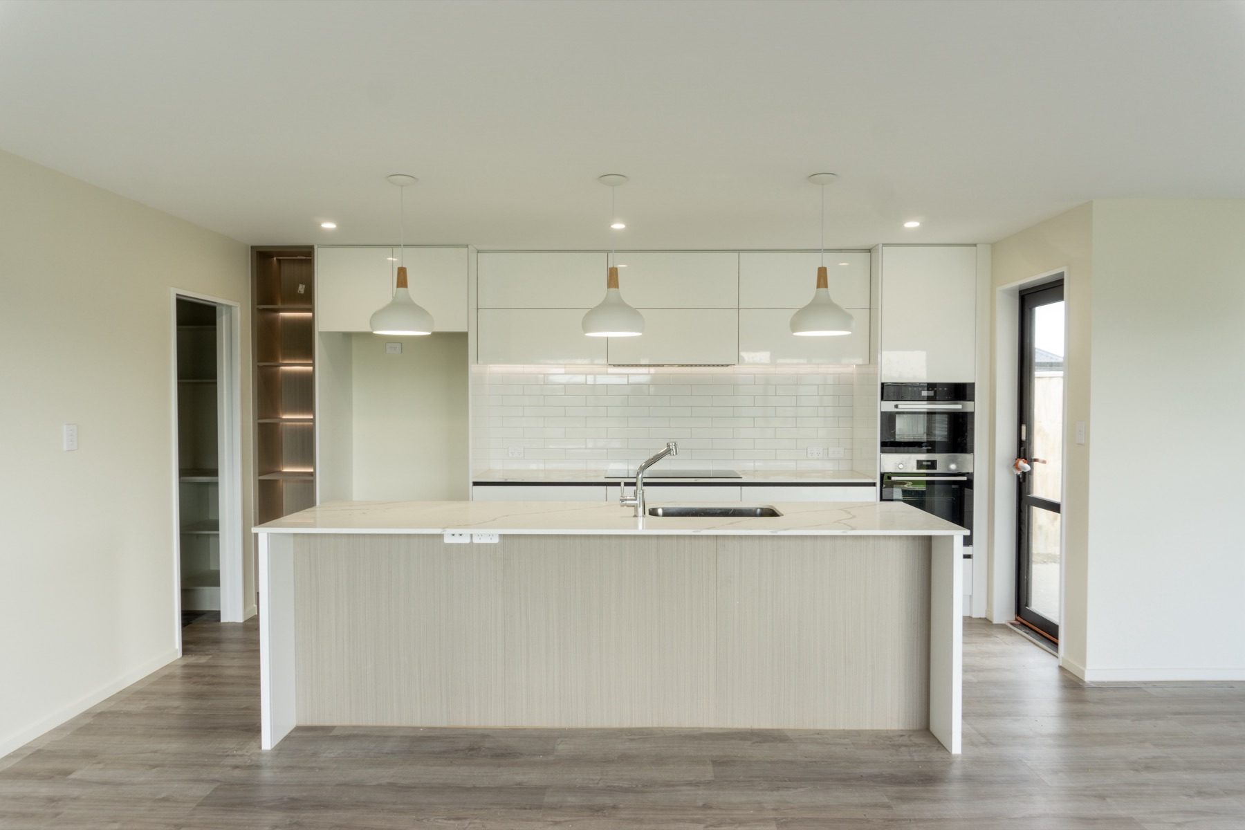 Kitchen and dining in the Rapere Street home, with a stone-topped island, white subway-tiled splashback, wall ovens and a walk-in scullery beyond.