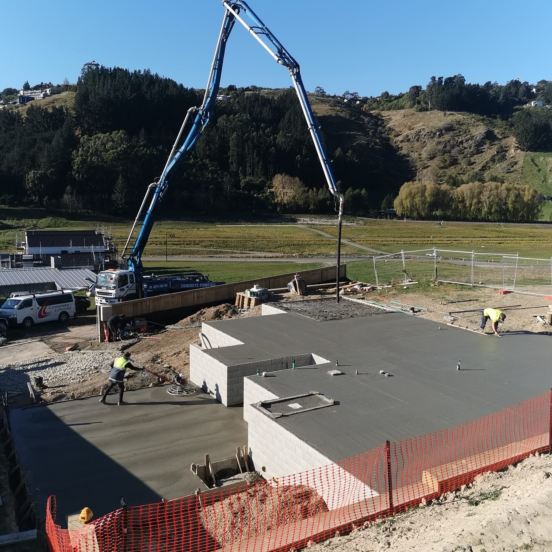 Two of the JSR crew floating a freshly poured floor slab, with the concrete pump boom reaching over the site from the road.