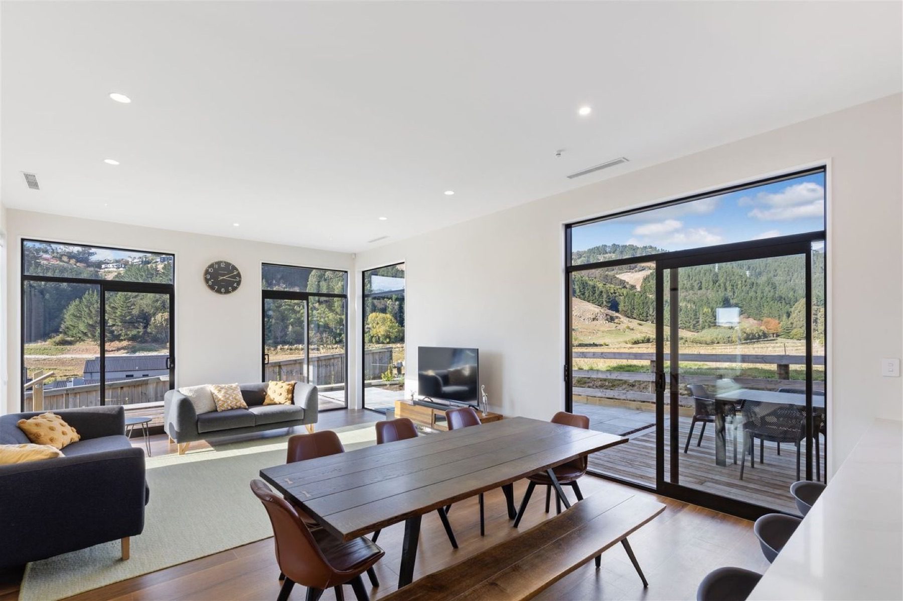 Open-plan living and dining at Round Hill Rise, with sliding doors to the deck and full-height glazing on two sides.
