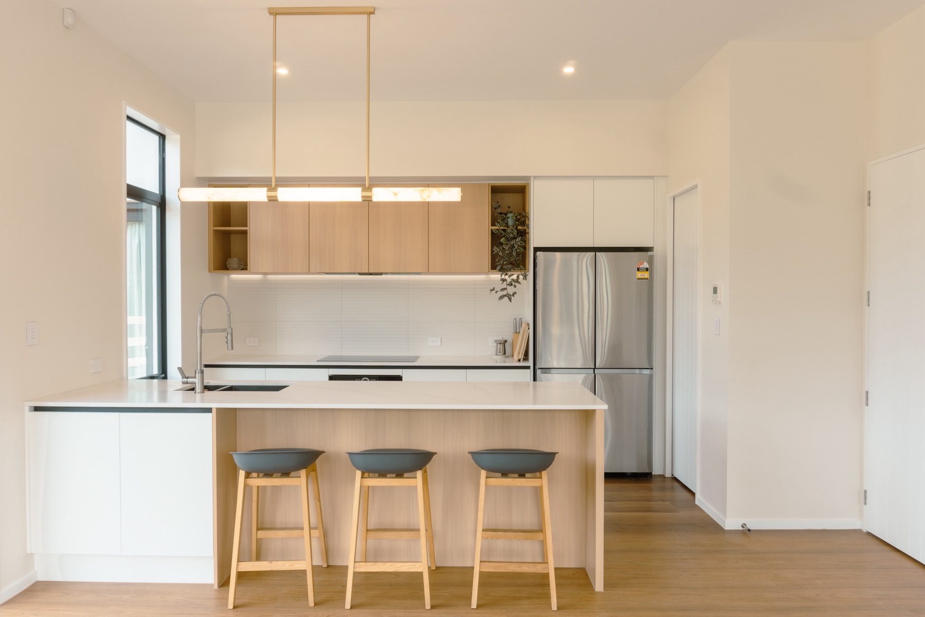 Kitchen at Round Hill Rise: oak overhead cabinetry with open end shelves, an induction cooktop, and three navy stools at the oak-fronted island.