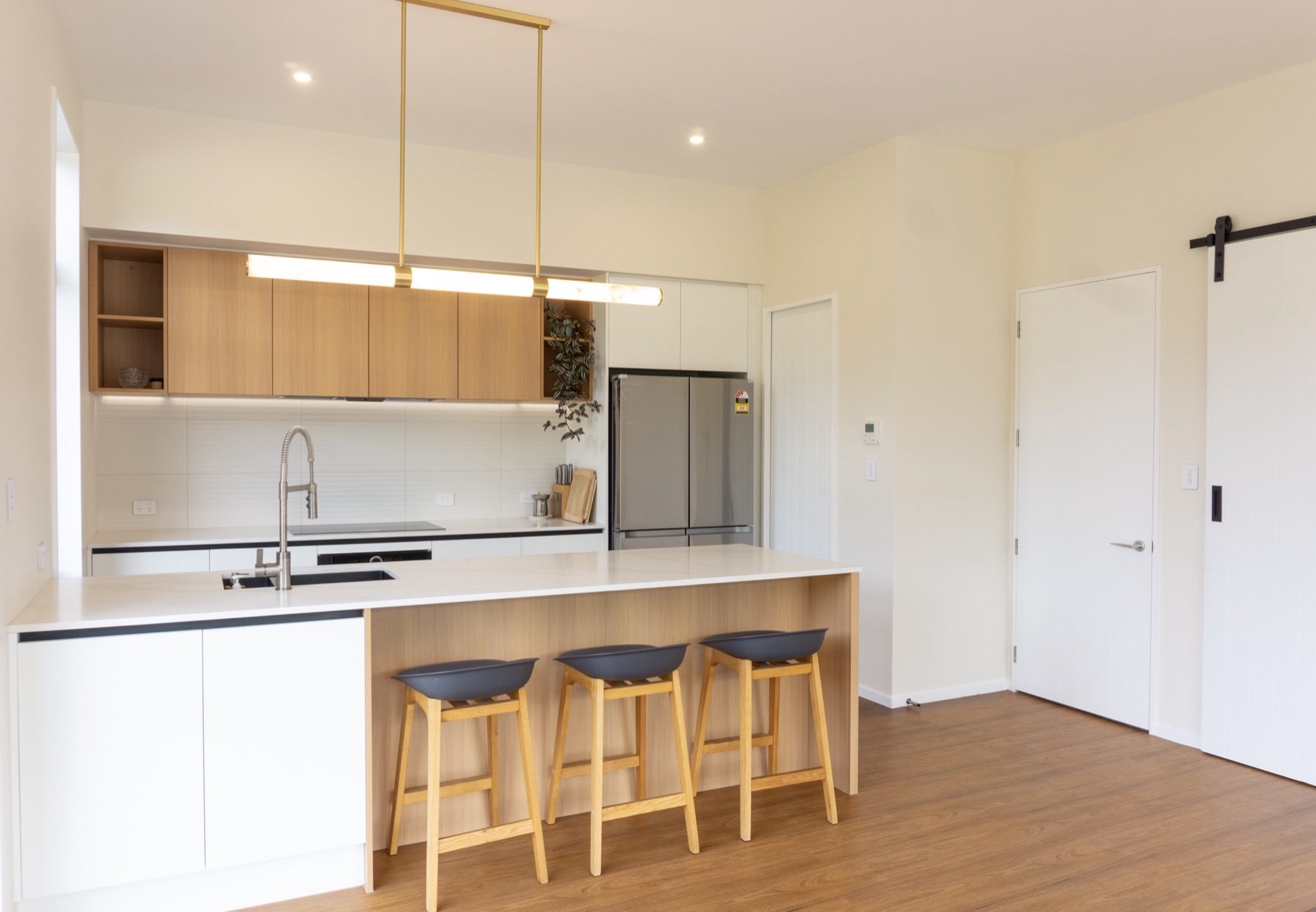Wider view of the Round Hill Rise kitchen, with the island run in the foreground and a black barn-slider door to the scullery beyond.