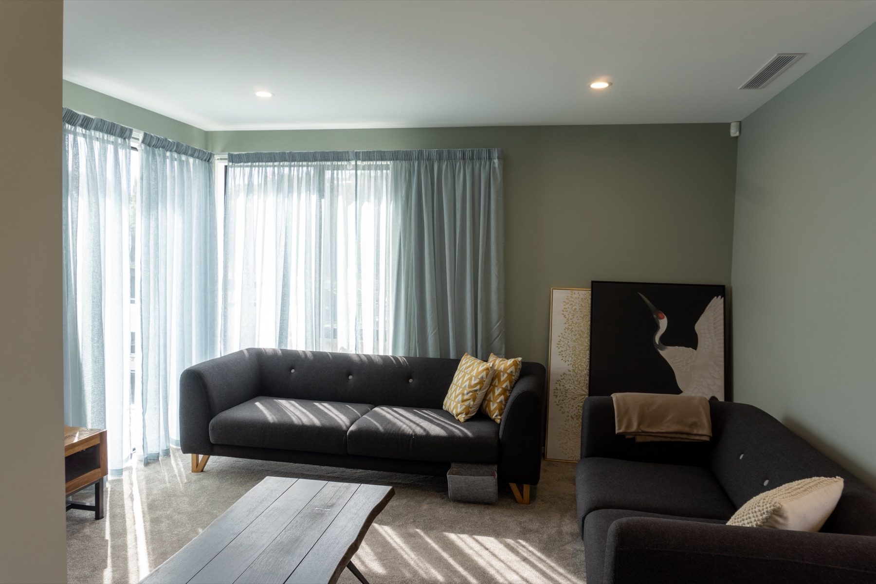 The second living room, painted sage green, with two charcoal sofas and sheer curtains drawn across a corner window.
