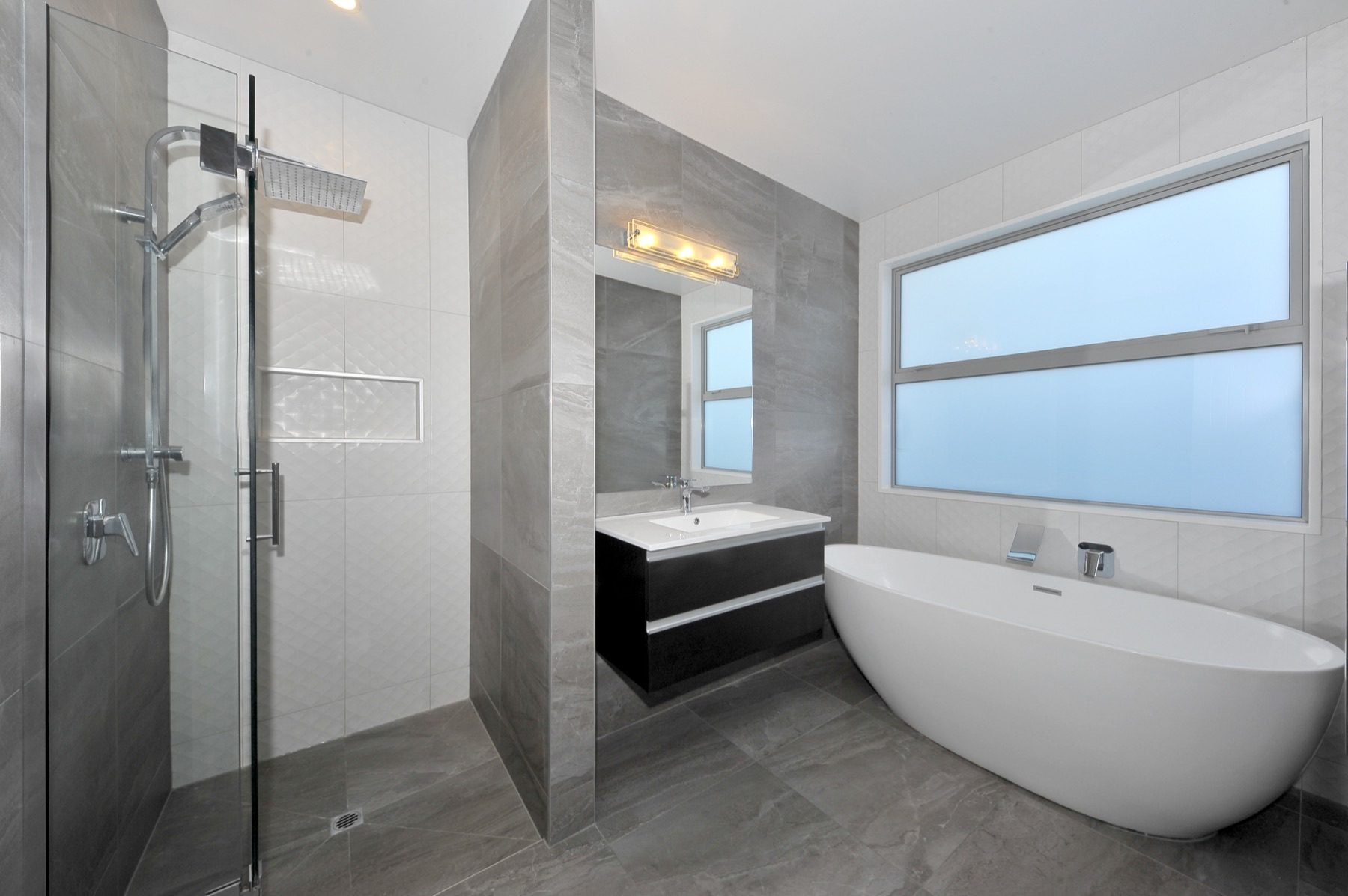 The fully tiled family bathroom, with a freestanding oval bath, a separate walk-in shower and a black floating vanity.