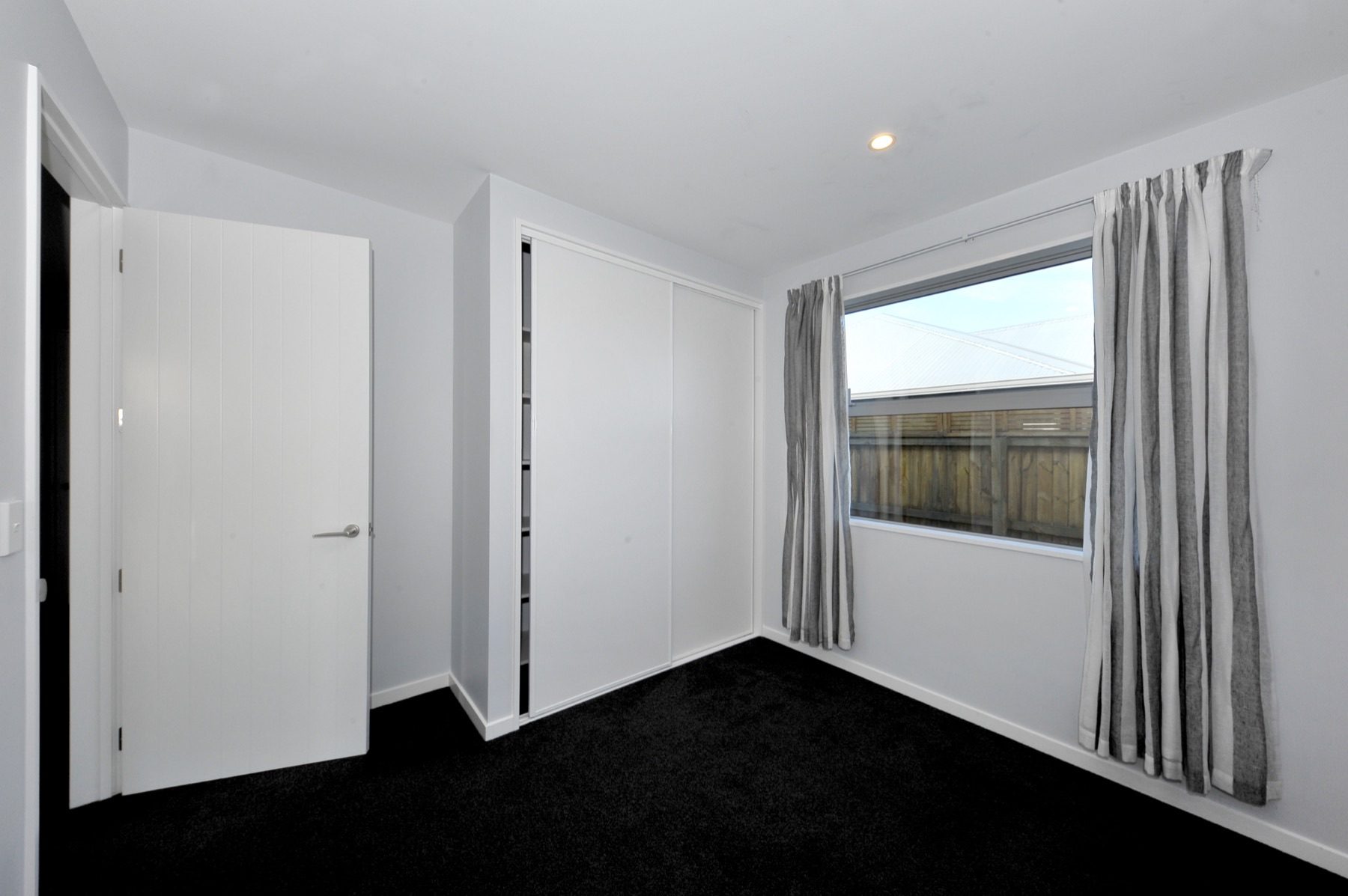 Bedroom at Vernon Drive with sliding wardrobe doors and a window to the boundary planting.