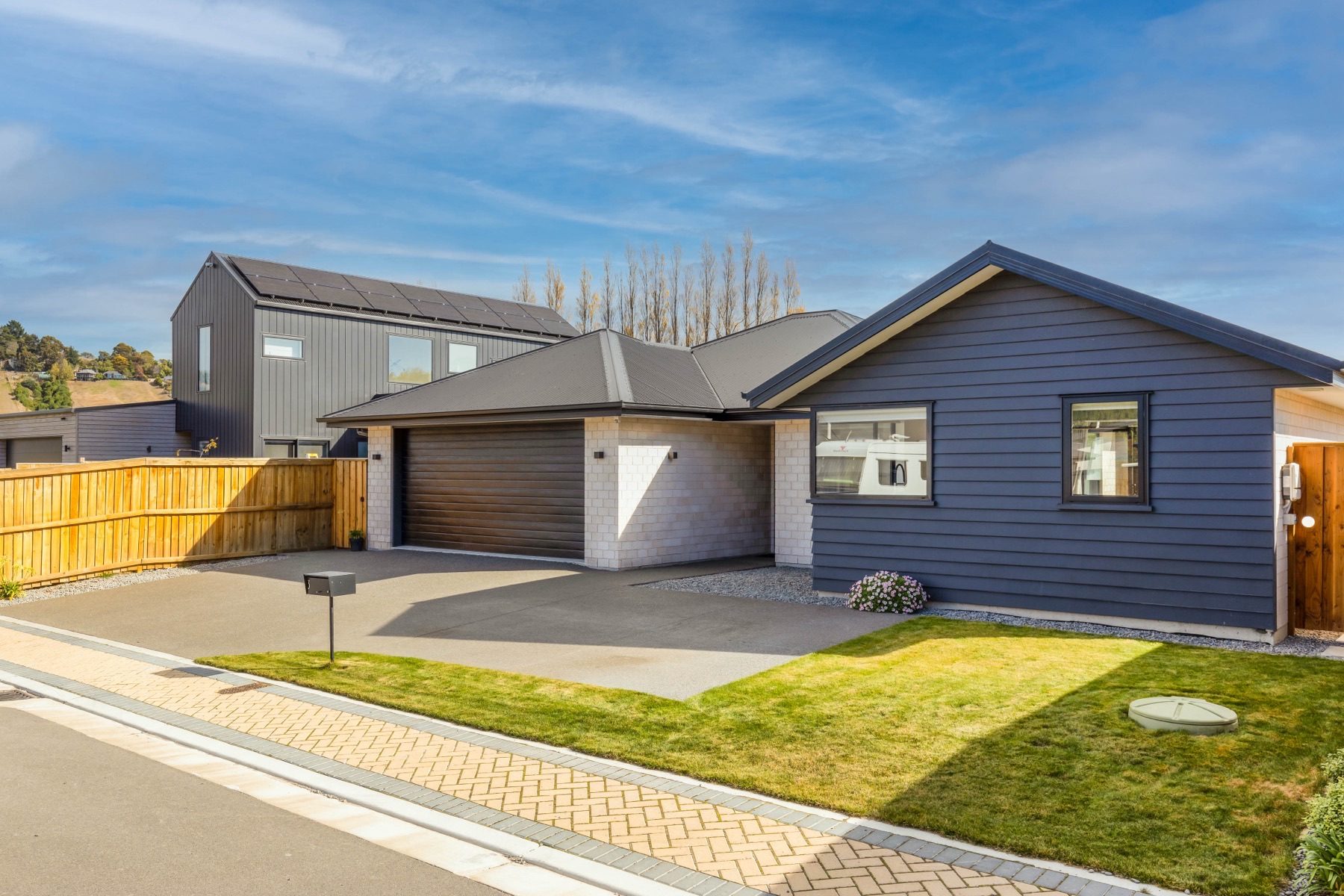 Front elevation of the Old Stone Lane home from the street, with dark weatherboard and pale block under a dark hip roof, and a paved driveway to the garage.