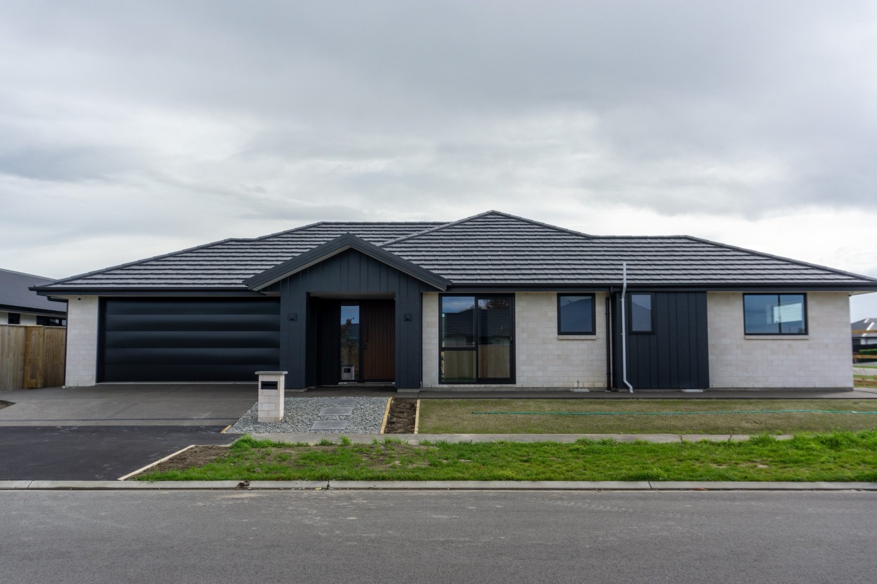 Front elevation of the Rapere Street home in Rolleston: pale brick, a dark tiled hip roof and a dark board-and-batten gable over the entry.