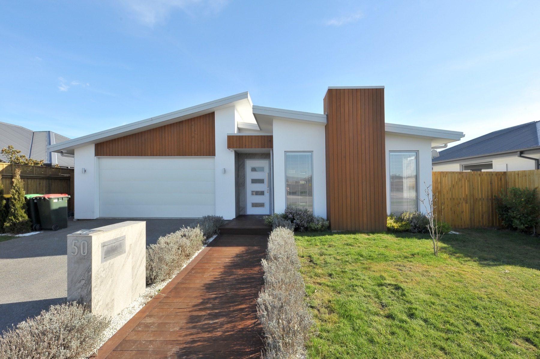 Street elevation of the Vernon Drive house, with its cedar-clad entry tower, white render and opposing mono-pitch roof planes.